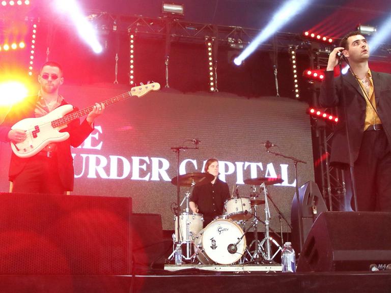 Die irische Band The Murder Capital steht auf einer Bühne, hinter der Band eine Projektion mit dem Namen der Band. 