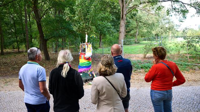 Mehrere Menschen stehen an der Gedenk-Stätte im Berliner Bezirk Mitte. Der Baum steht schräg. Jemand hat ihn aus dem Boden gerissen.