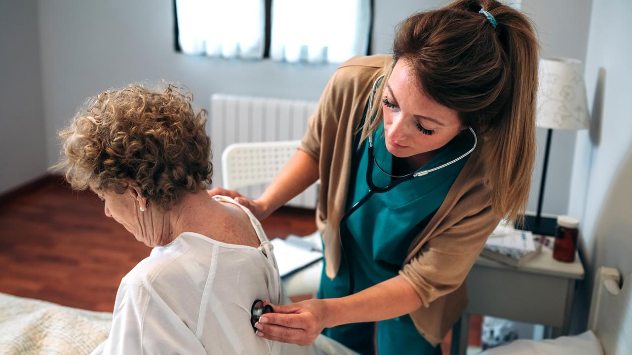 Eine Seniorin wird von einer jungen Pflegerin mit einem Stethoskop untersucht