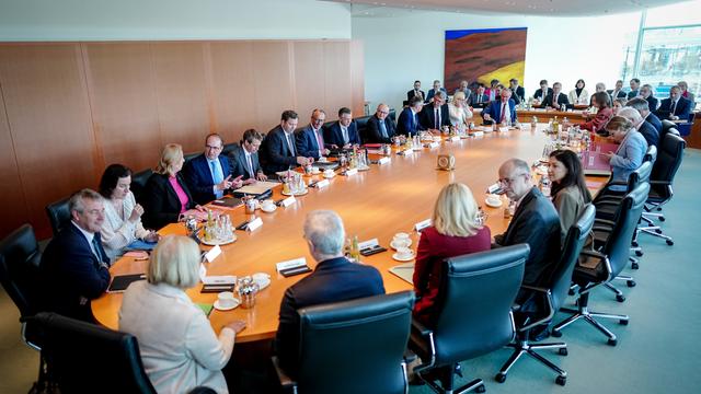Die Mitglieder von der Bundes-Regierung sitzen bei der Kabinetts-Sitzung alle an einem Tisch zusammen. 