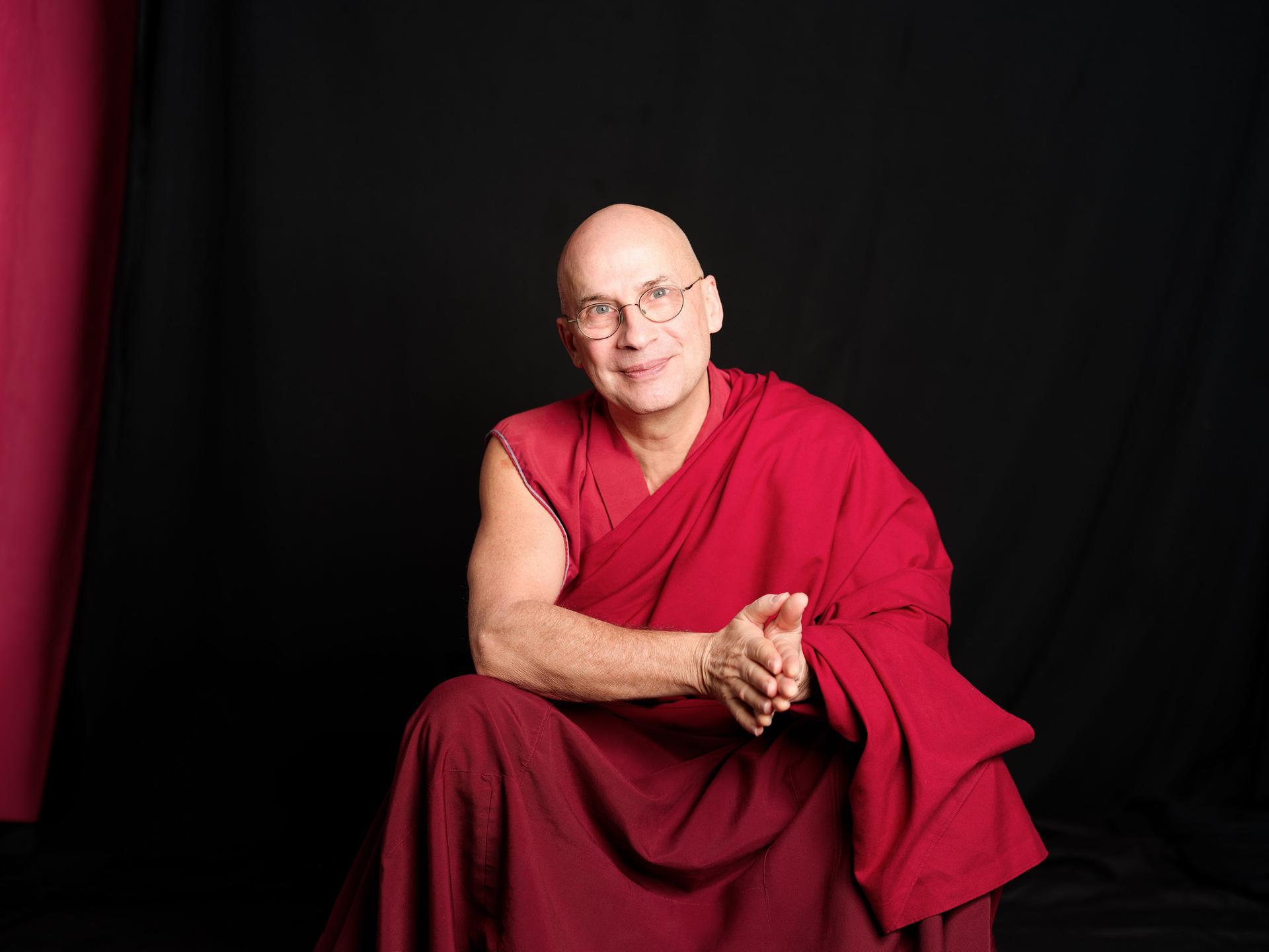 Tenzin Peljor sitzt in traditionell buddhistischem Gewand vor einem schwarzen Hintergrund und schaut freundlich in die Kamera.