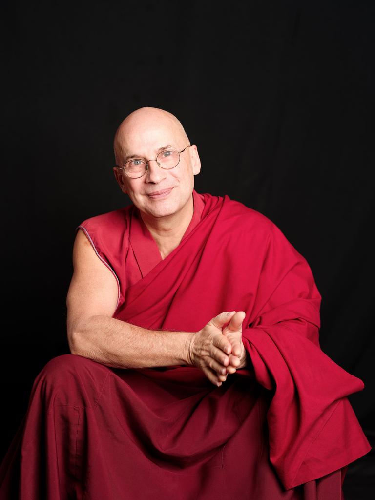 Tenzin Peljor sitzt in traditionell buddhistischem Gewand vor einem schwarzen Hintergrund und schaut freundlich in die Kamera.