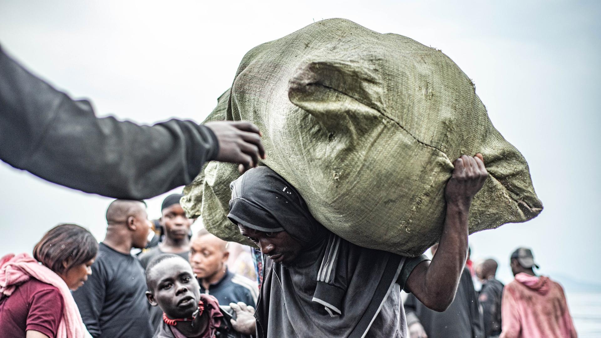 Mann mit schwerem Sack auf dem Rücken läuft gekrümmt am Hafen von Nzulo in der Nähe von Goma (DR Kongo)