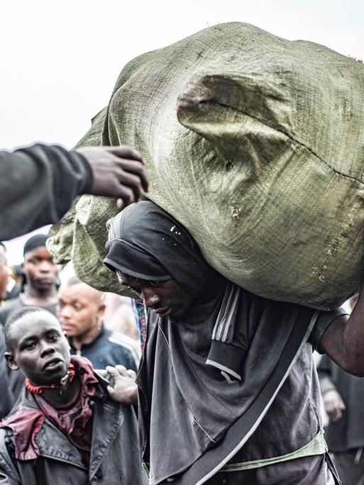 Mann mit schwerem Sack auf dem Rücken läuft gekrümmt am Hafen von Nzulo in der Nähe von Goma (DR Kongo)