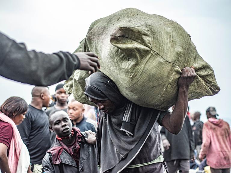 Mann mit schwerem Sack auf dem Rücken läuft gekrümmt am Hafen von Nzulo in der Nähe von Goma (DR Kongo)