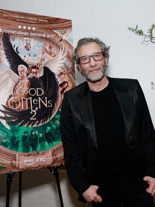 Der britische Schrifsteller und Drehbuchautor Neil Gaiman steht vor einem Plakataufsteller der Amazon-Prime-Serie "Good Omens", deren zweite Staffel beworben wird.