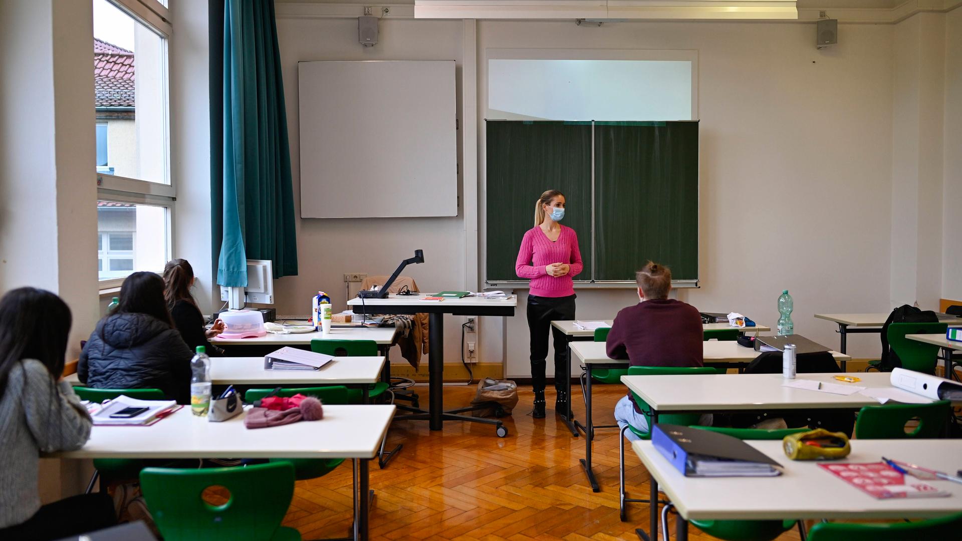 Eine Lehrerin mit Mundschutz steht an der Tafel. Von den Schülern ist jeder Tisch nur einzeln besetzt.