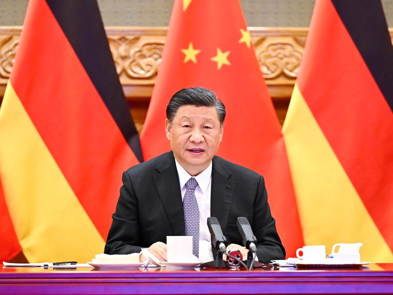 Xi Jinping sitzt vor deutschen und chinesischen Fahnen