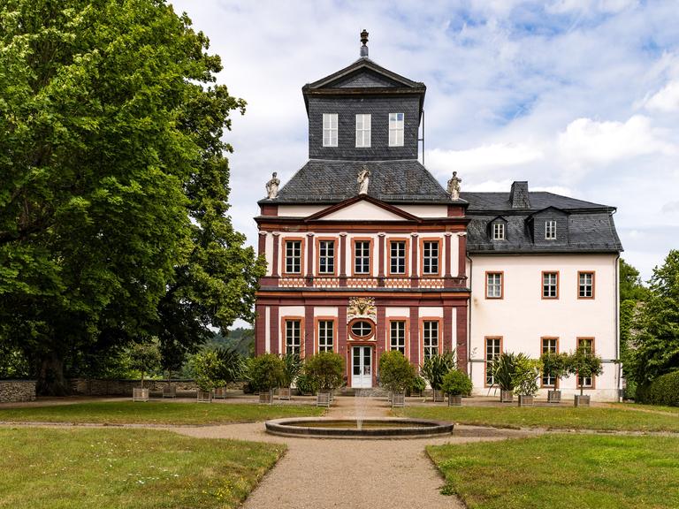 Hinter einem Springbrunnen steht das Schloss Schwarzburg in einem Park.