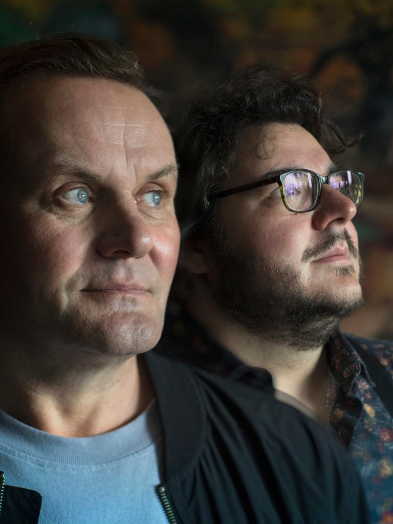 Devid Striesow und Axel Ranisch stehen in einem dunklen Raum und schauen zur Seite.