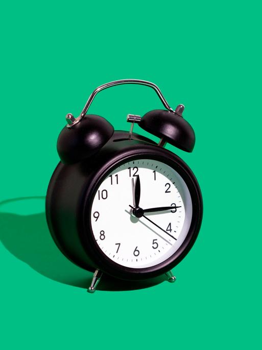 Ein schwarzer Wecker vor einem grünen Hintergrund