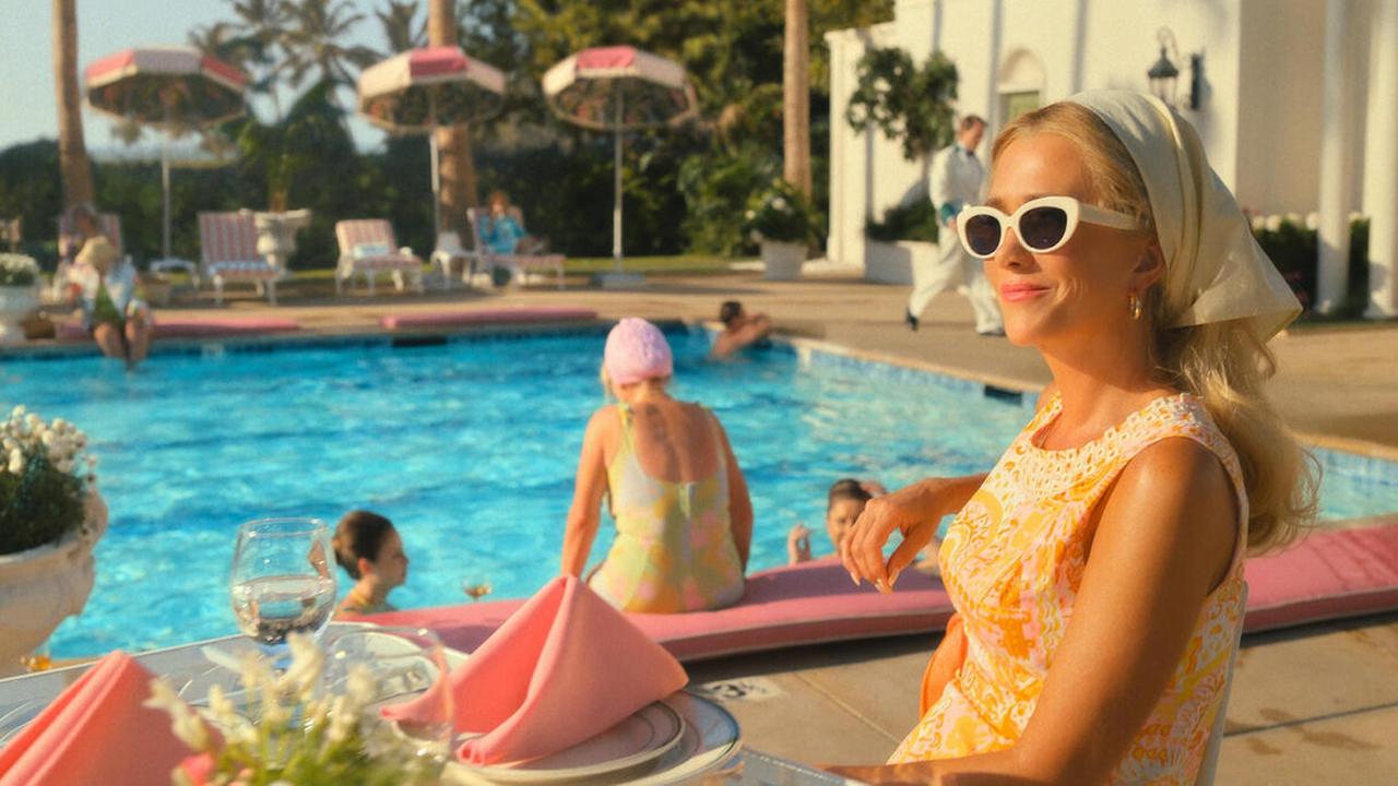 Im Still aus "Palm Royale" sitzt Kristen Wiig in einem Club an einem Pool.
