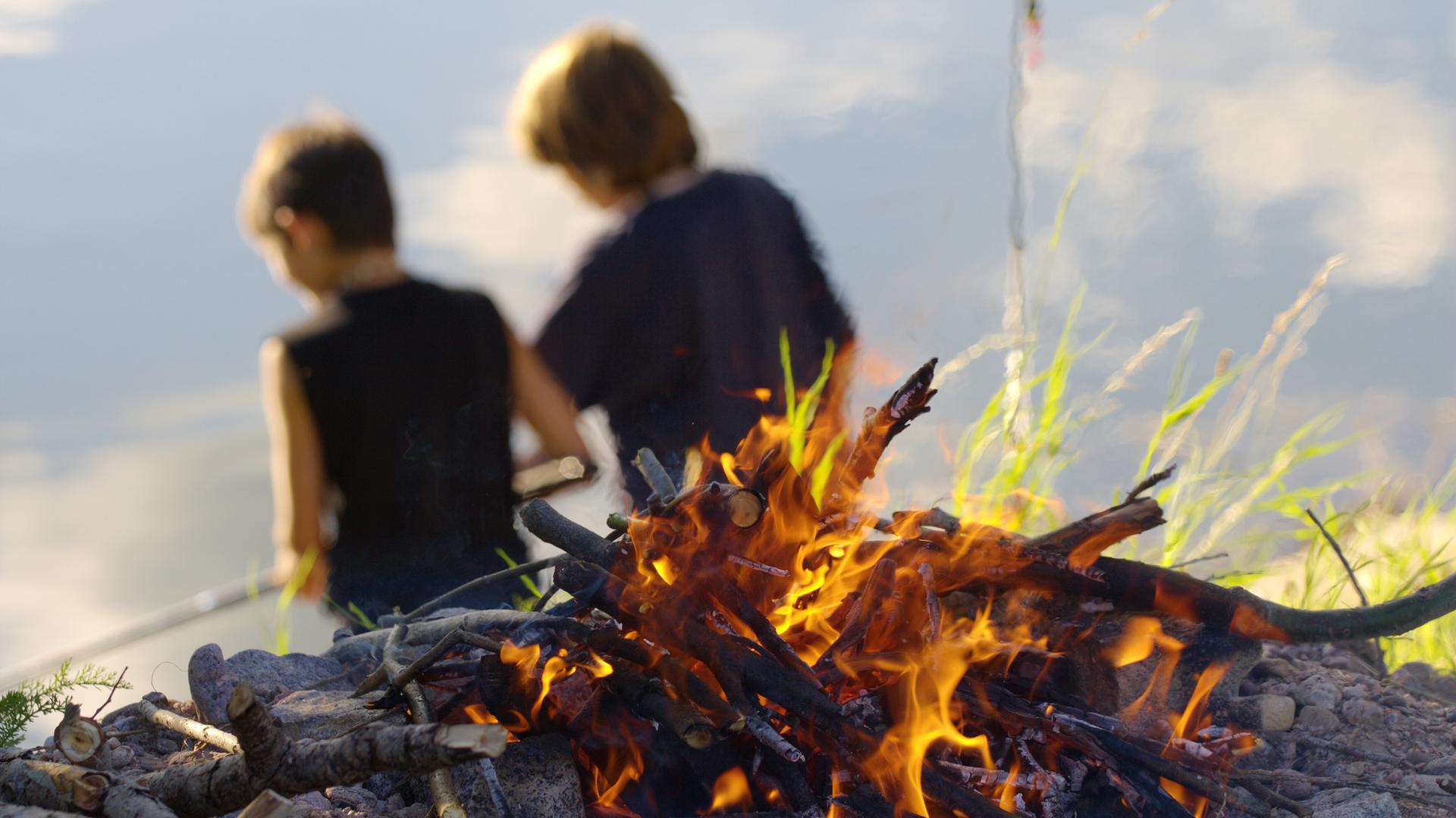 Zwei Pfadfinder in der Rückansicht mit einem Lagerfeuer im Vordergrund. Zwei Pfadfinder in der Rückansicht mit einem Lagerfeuer im Vordergrund.
