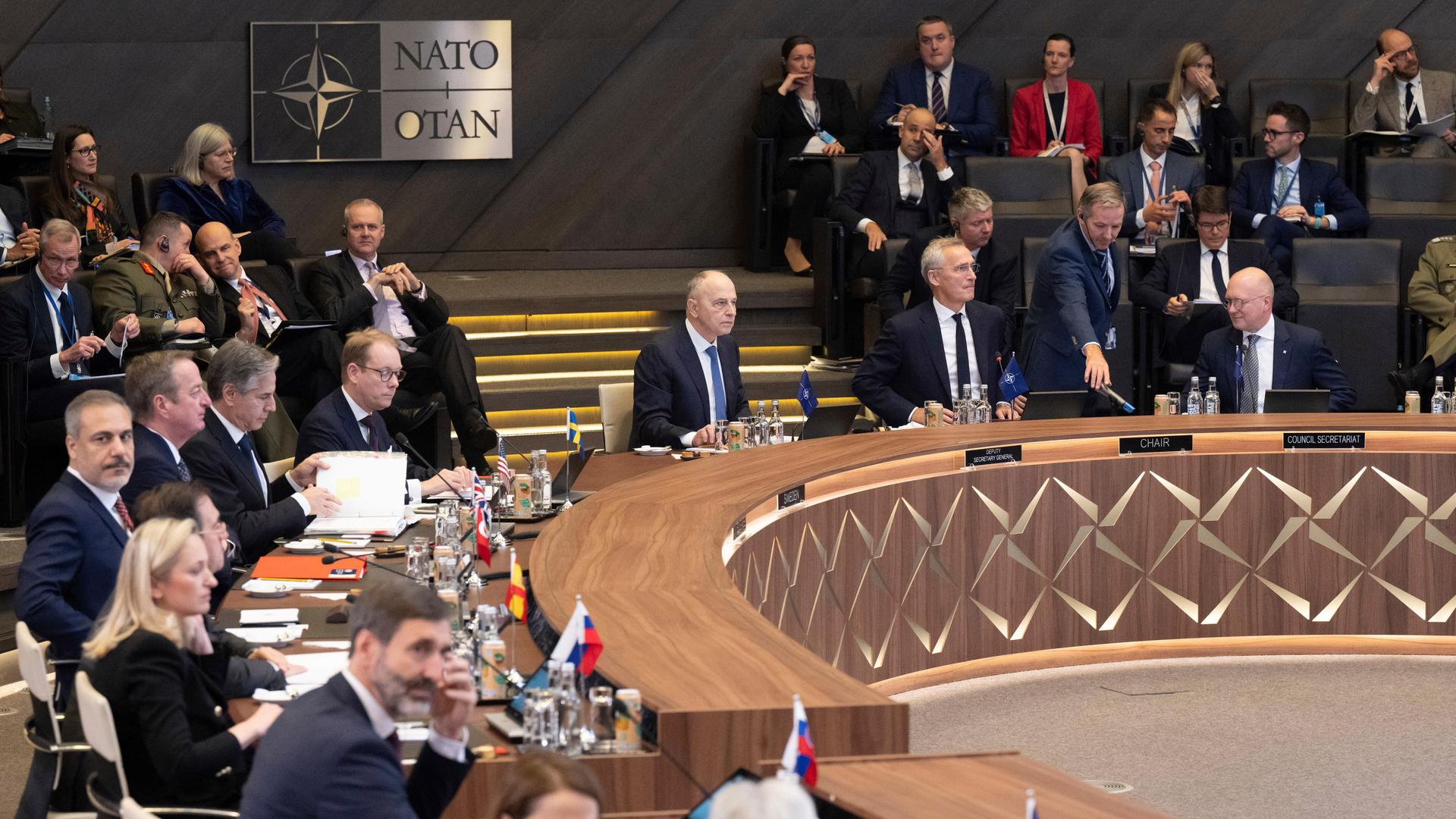 NATO-Generalsekretär Stoltenberg sitzt gemeinsam mit anderem Personen im Sitzungssaal der NATO in Brüssel.