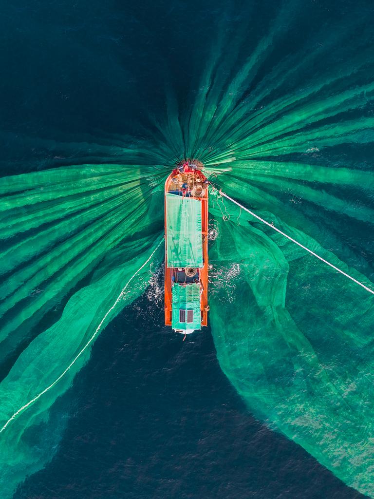 Drohnenfoto mit Blick auf einen Fischtrawler beim Sardellenfang. Aus der Vogelperspektive sind die Netze deutlich im Wasser zu erkennen. 
