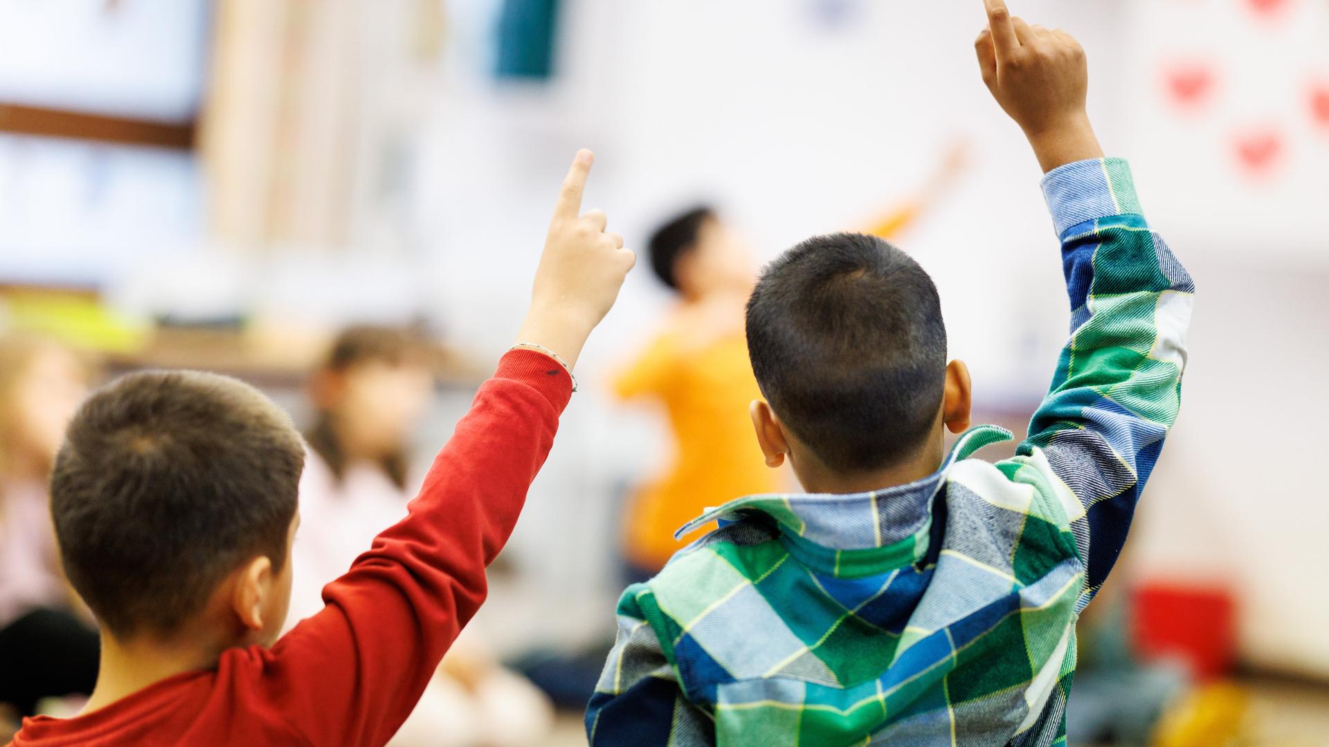 Schüler einer zweiten Klasse einer Grundschule sitzen während des Unterrichts in einem Kreis auf dem Boden des Klassenzimmers zusammen und melden sich.