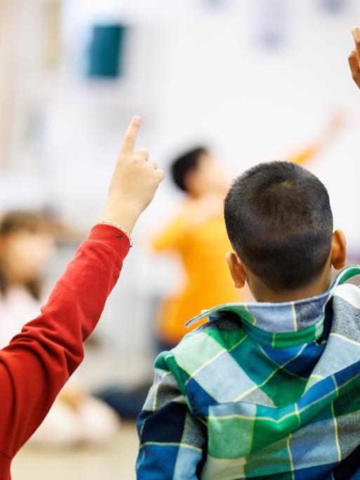 Schüler einer zweiten Klasse einer Grundschule sitzen während des Unterrichts in einem Kreis auf dem Boden des Klassenzimmers zusammen und melden sich.