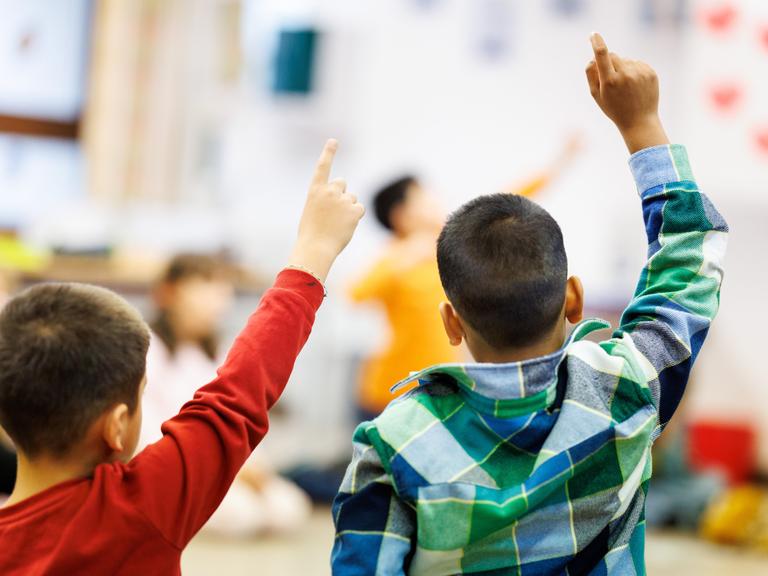 Schüler einer zweiten Klasse einer Grundschule sitzen während des Unterrichts in einem Kreis auf dem Boden des Klassenzimmers zusammen und melden sich.