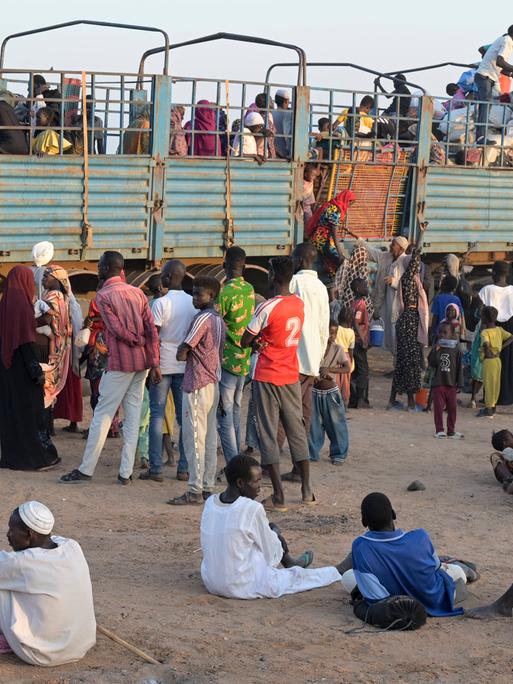 Dutzende sudanesische Flüchtlinge stehen auf sandigem Boden vor einem LKW, um aufzusteigen.