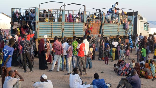 Dutzende sudanesische Flüchtlinge stehen auf sandigem Boden vor einem LKW, um aufzusteigen.