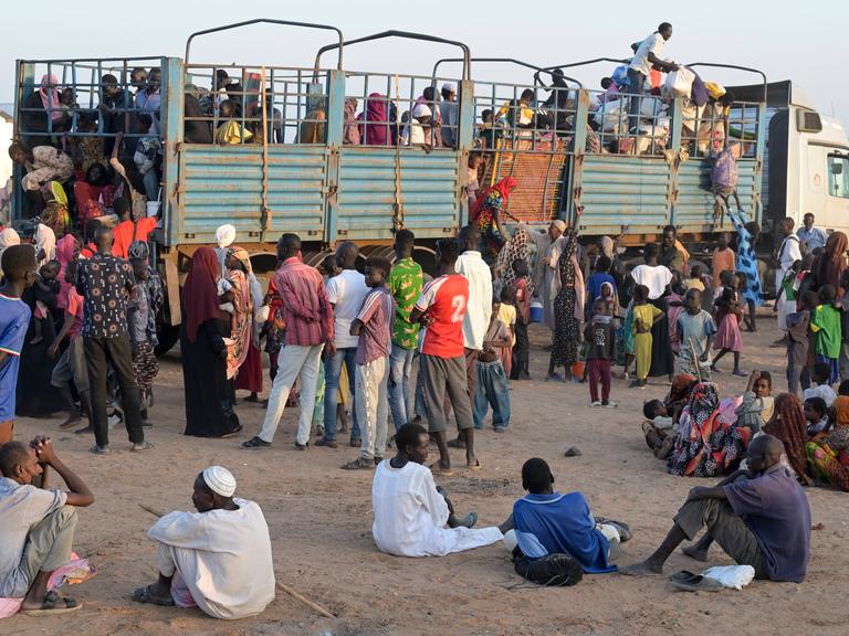 Dutzende sudanesische Flüchtlinge stehen auf sandigem Boden vor einem LKW, um aufzusteigen.