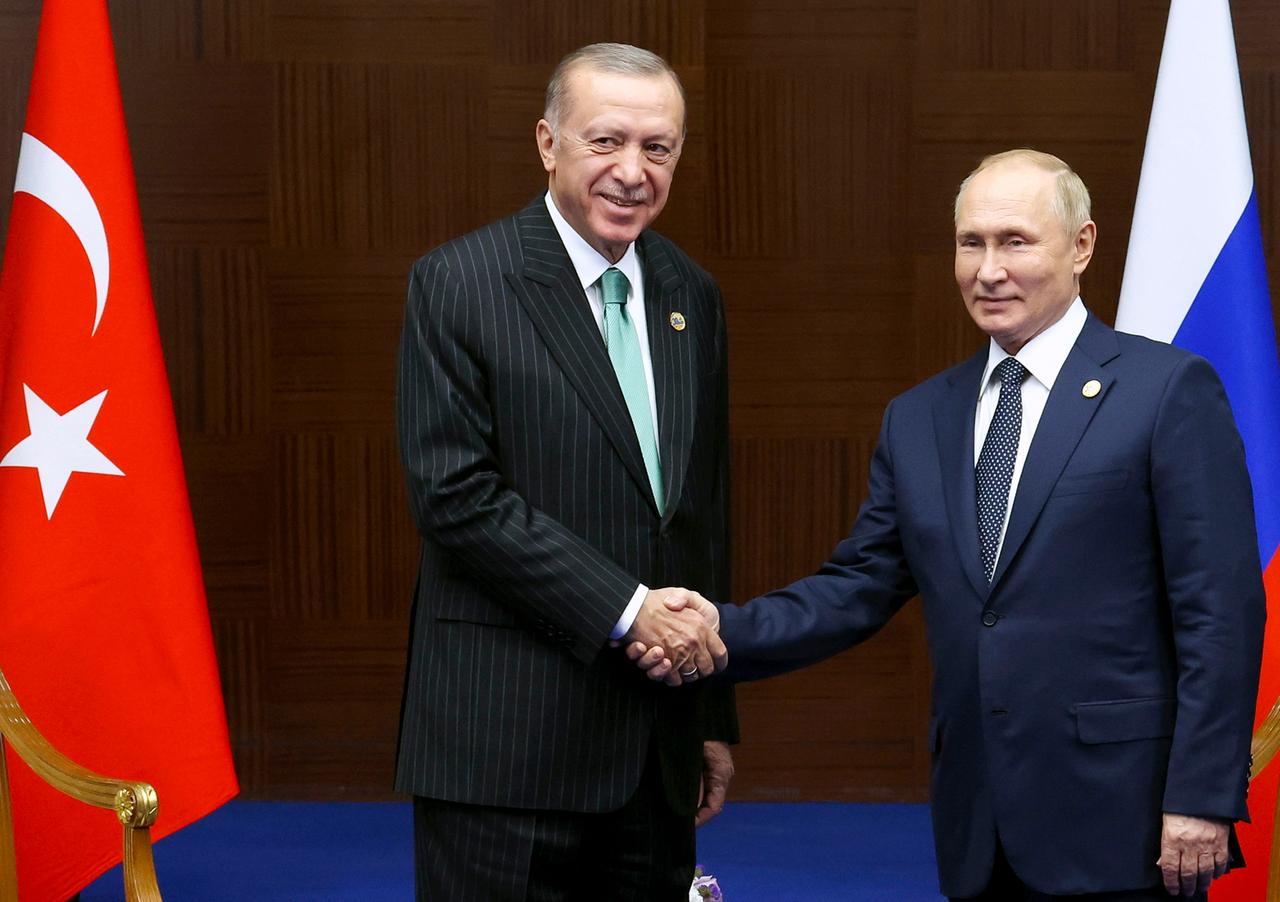 Der türkische Präsident Erdogan (l.) gibt Russlands Staatschef Putin bei einem Treffen im Oktober 2022 die Hand, dahinter die Flaggen der beiden Länder.