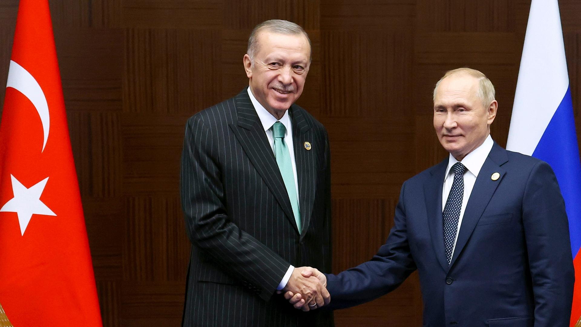 Der türkische Präsident Erdogan (l.) gibt Russlands Staatschef Putin die Hand, dahinter die Flaggen der beiden Länder.