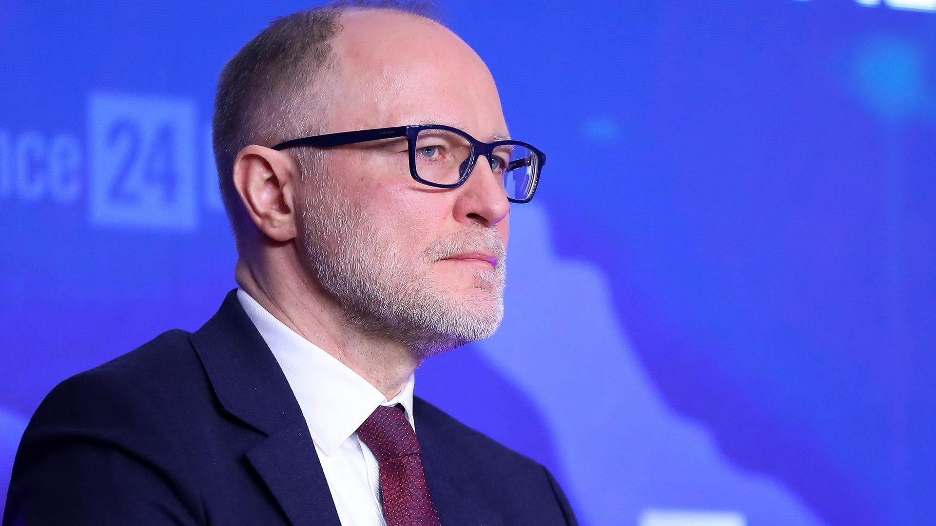Nahaufnahme von Andris Spruds bei den "Defence24 Days" in Warschau. Er steht vor einem blauen Hintergrund und blickt nach rechts aus dem Bild. 