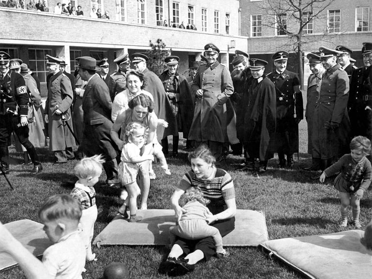 Ehrengäste des Führers auf dem Reichssportfeld sehen zu, wie Frauen mit Kleinkindern spielen. Im Hintergrund Offiziere der Wehrmacht, der Allgemeinen SS, des Auswärtigen Amts und einer ausländischen Delegation.