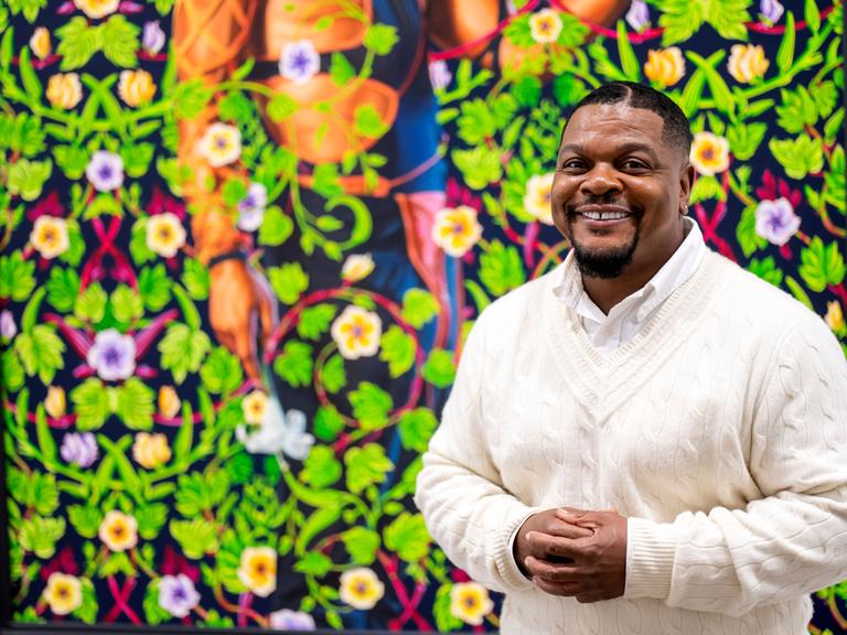 Kehinde Wiley vor einem einer Bilder mit grünen Blätterranken und Blüten Kehinde Wiley vor einem einer Bilder mit grünen Blätterranken und Blüten
