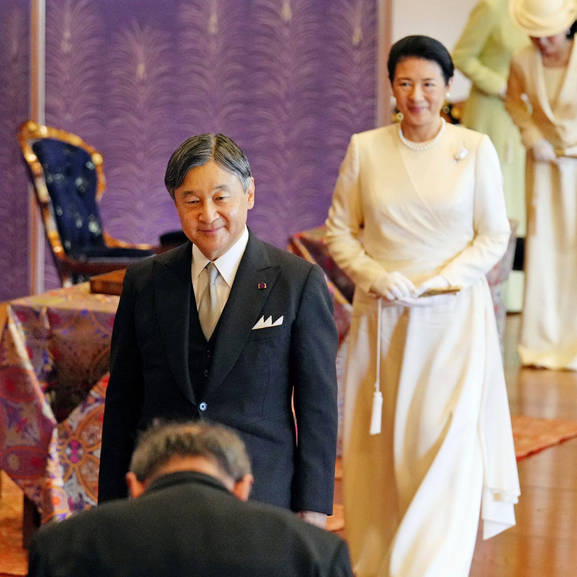 Kaiser Naruhito steht vor seiner Gattin Masako beim Empfang von Gästen. Im Vordergrund ein Mann, der sich verneigt.