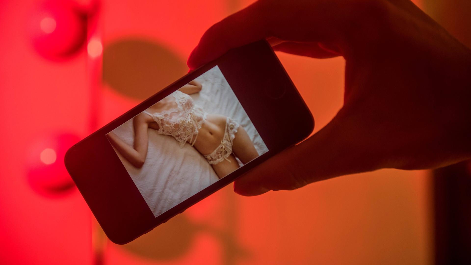 Auf einem Handydisplay sind Teile eines Frauenkörpers in Dessous zu sehen.