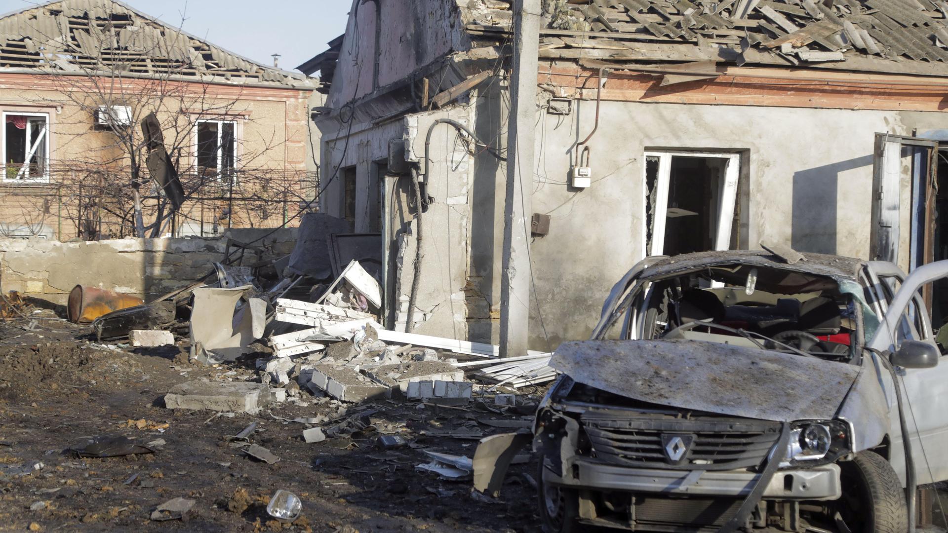 Das Bild zeigt zerstörte Häuser und ein zerstörtes Auto in einem Kriegsgebiet.