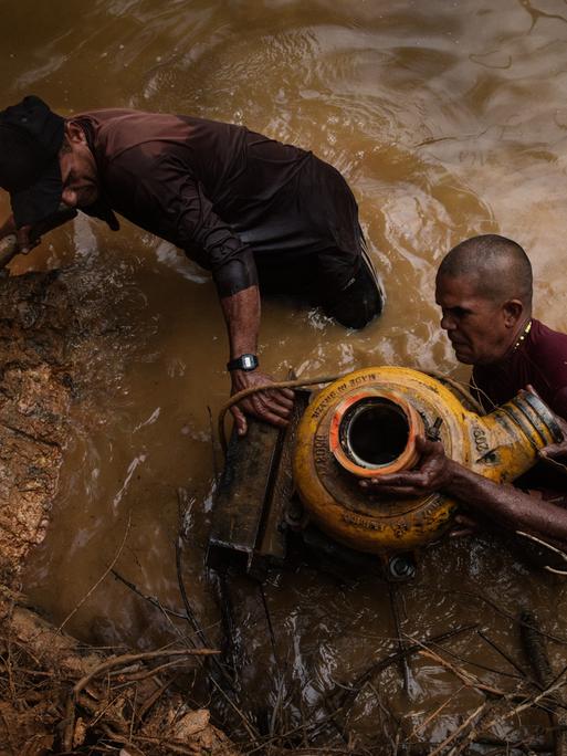 Illegale Goldwäscher bergen eine Maschine, die sie zuvor bei einer Polizeirazzia ins Wasser geworfen haben, um sie zu verstecken.