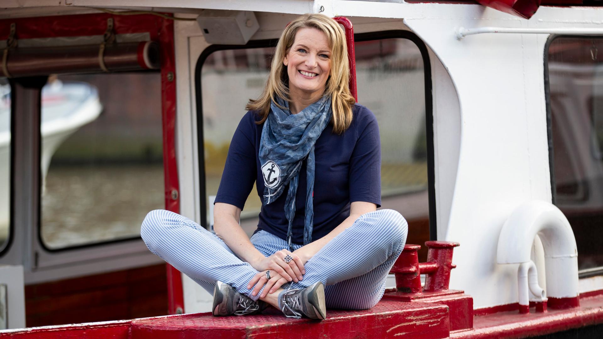 Tour-Guide Maike Brunk sitzt im Schneidersitz auf einer rotlackierten Fläche eines Schiffes.