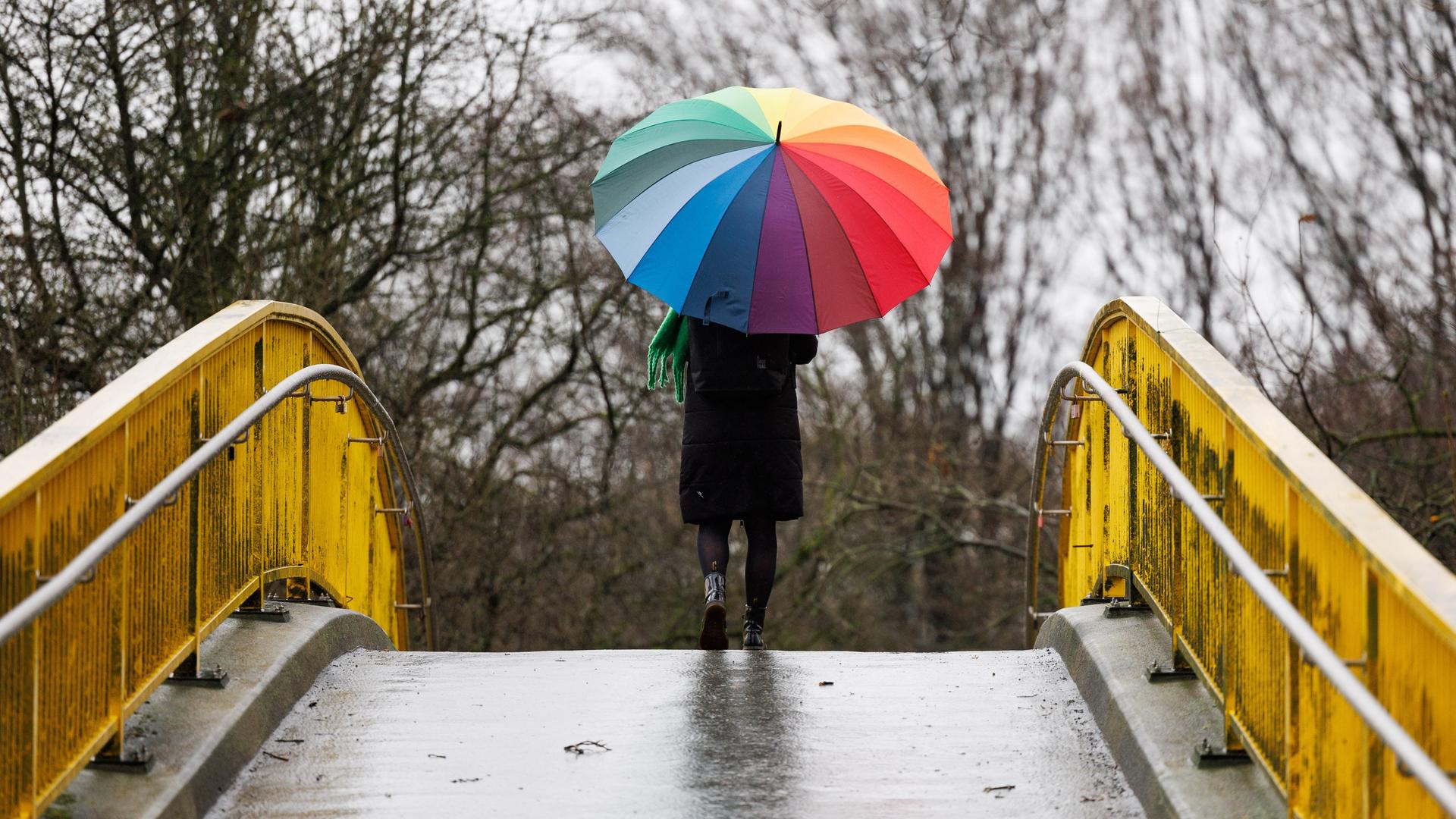Eine Frau geht mit einem bunten Regenschirm über eine Brücke.