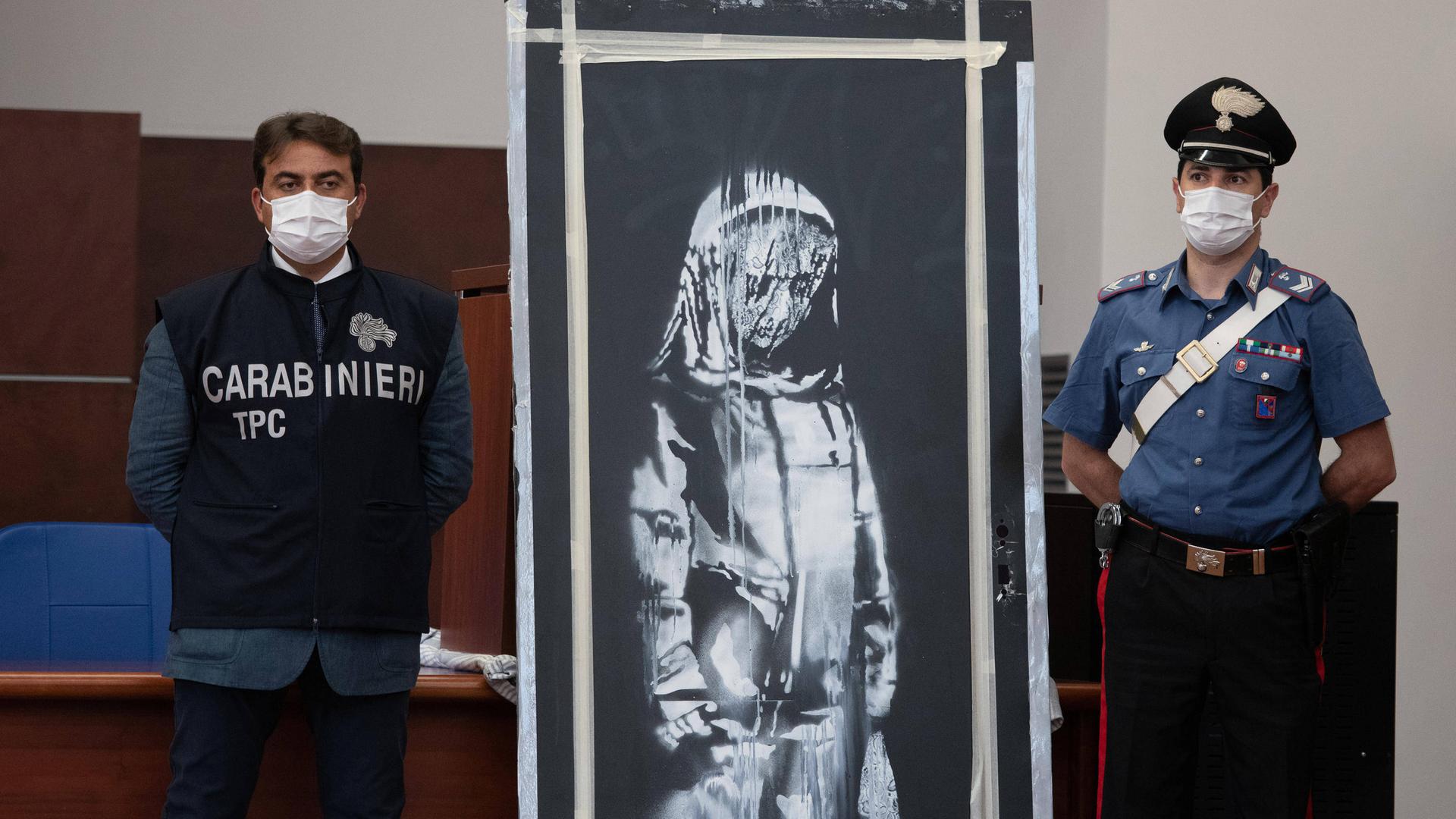 Zwei italienische Polizeibeamte stehen bei dem Banksy-Bild, das ein trauriges Mädchen zeigt. Zwei italienische Polizeibeamte stehen bei dem Banksy-Bild, das ein trauriges Mädchen zeigt.