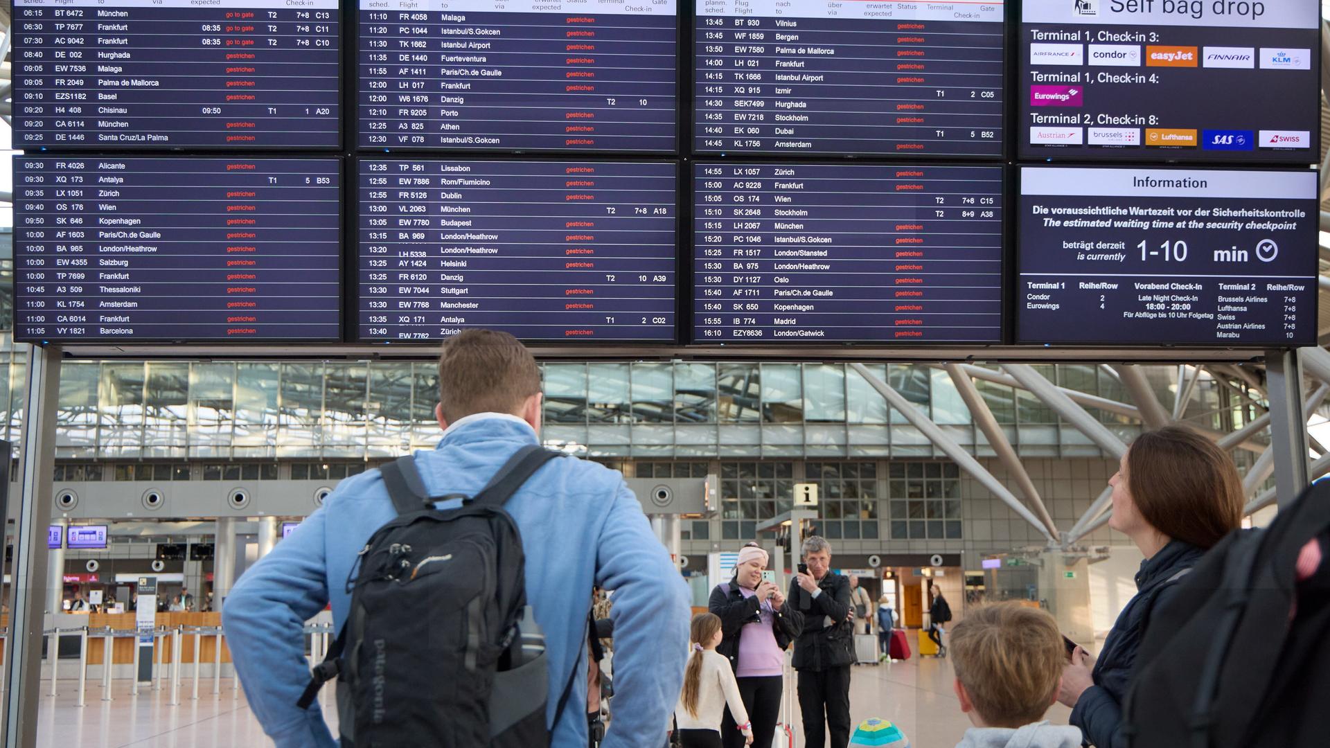 Die Anzeigetafeln im Flughafengebäude zeigen an, dass fast alle Flüge ausfallen. Davor stehen Reisende.