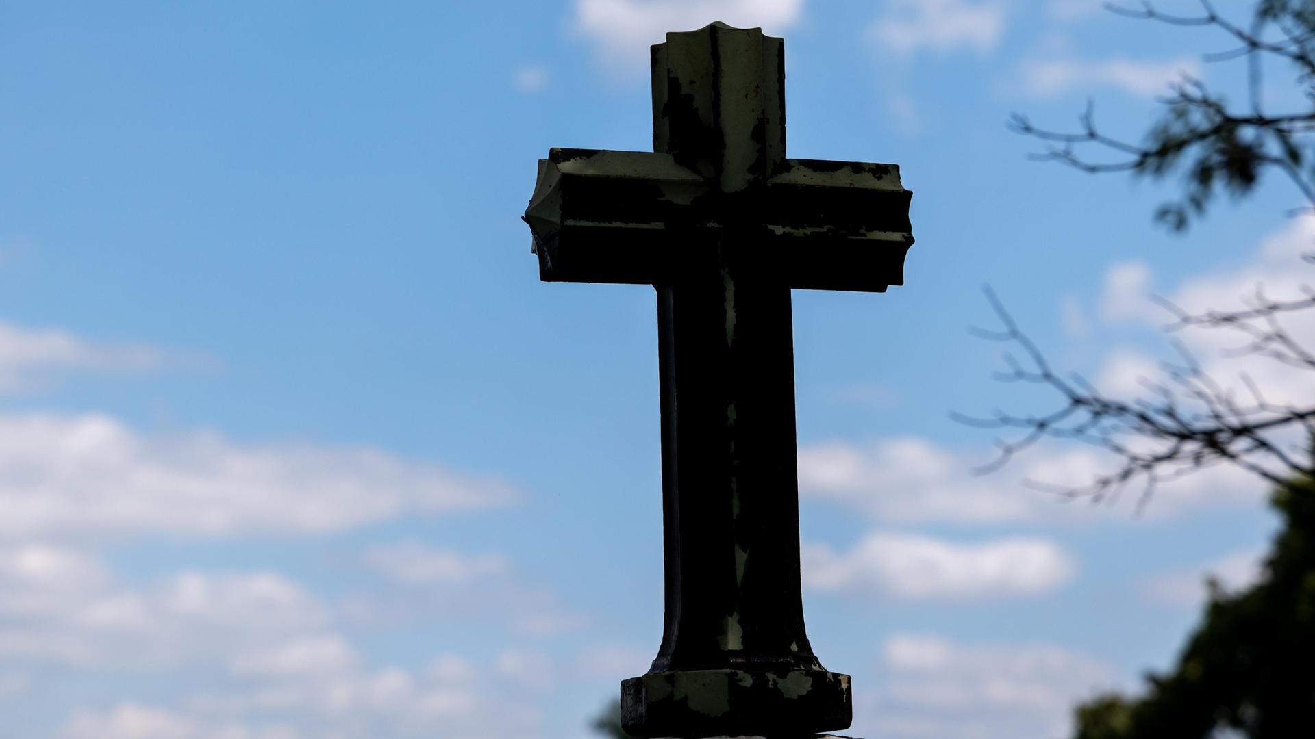Ein dunkles Kreuz als Silhouette vor blauem Himmel mit leichten Wolken Ein dunkles Kreuz als Silhouette vor blauem Himmel mit leichten Wolken