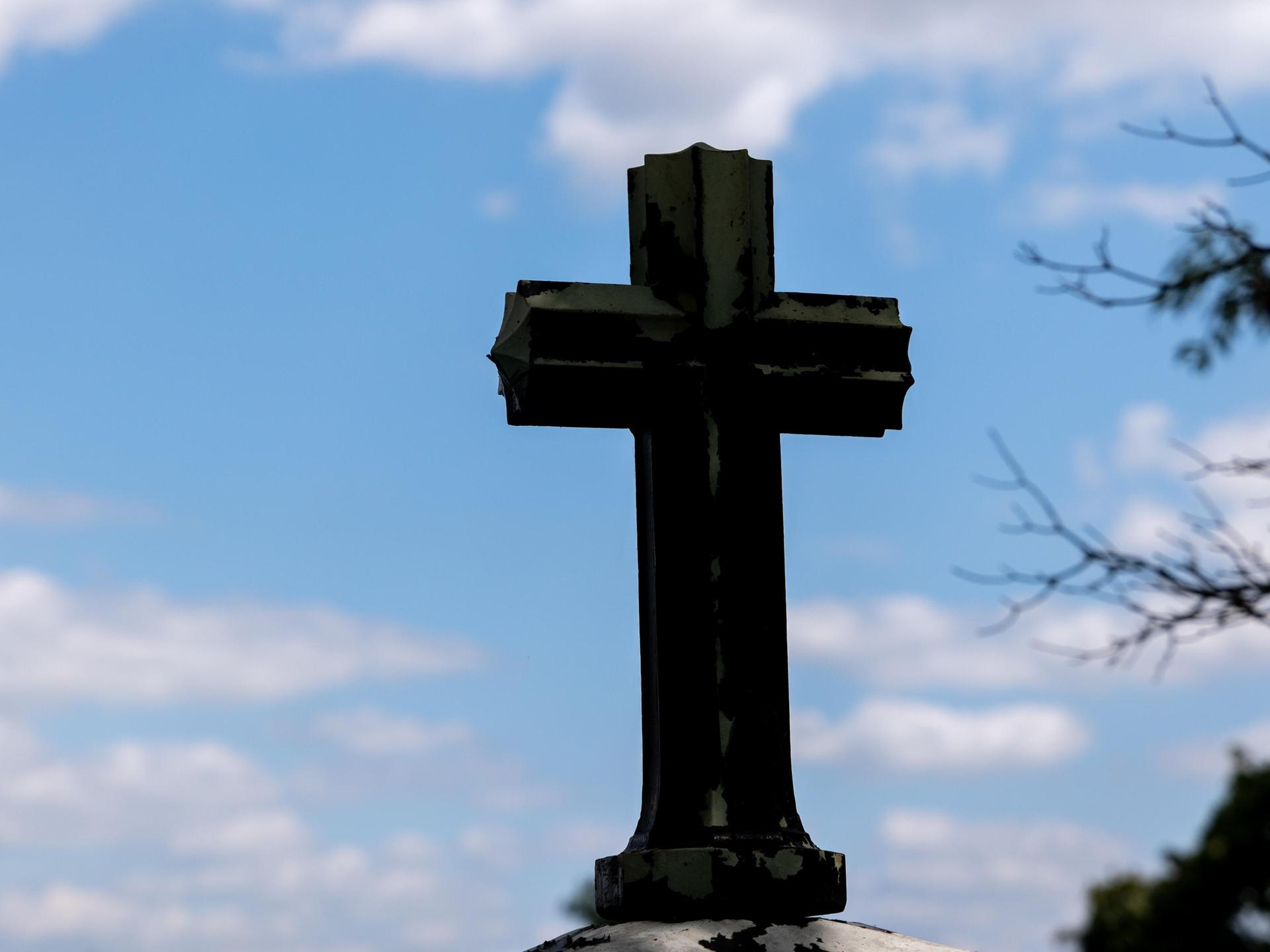 Ein dunkles Kreuz als Silhouette vor blauem Himmel mit leichten Wolken 