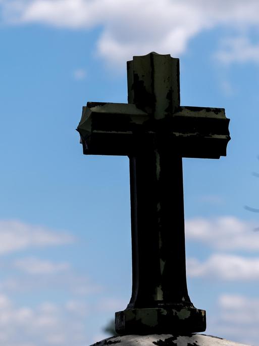 Ein dunkles Kreuz als Silhouette vor blauem Himmel mit leichten Wolken 