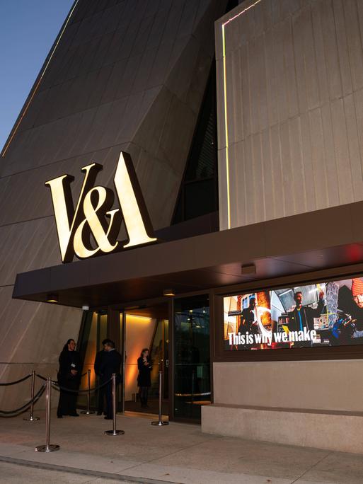 Das neue V&A East Museum in London. Es besteht aus viel Beton, über dem Eingang hängen in Gold die Buchstaben V&A.