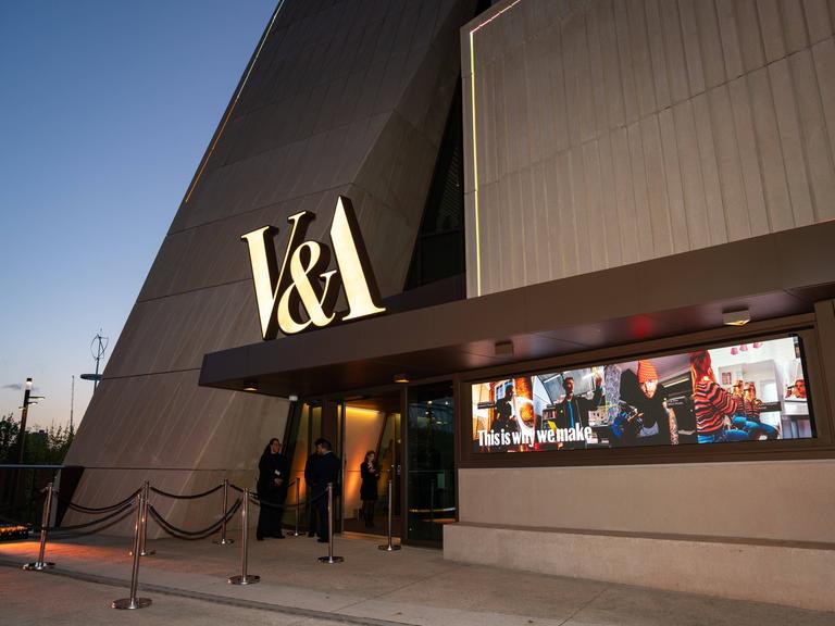 Das neue V&A East Museum in London. Es besteht aus viel Beton, über dem Eingang hängen in Gold die Buchstaben V&A.