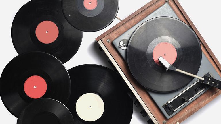 Fünf unbeschriftete Schallplatten liegen neben einem Schallplattenspieler, auf dem eine Platte abspielt.