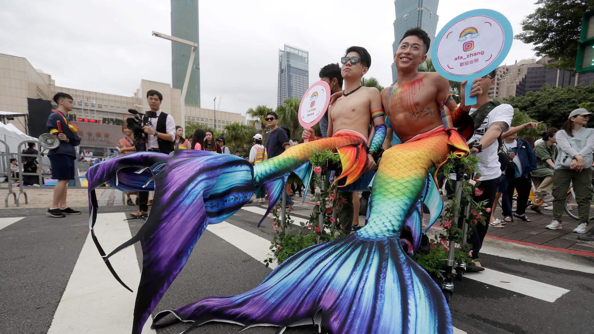 Menschen in Kostümen nehmen an der jährlichen Taiwan LGBTQ+ Pride-Parade teil. Im Bild sind zwei Männer mit nacktem Oberkörper zu sehen, die Meerjungfrauen-Schwänze in Regenbogenfarben tragen.
