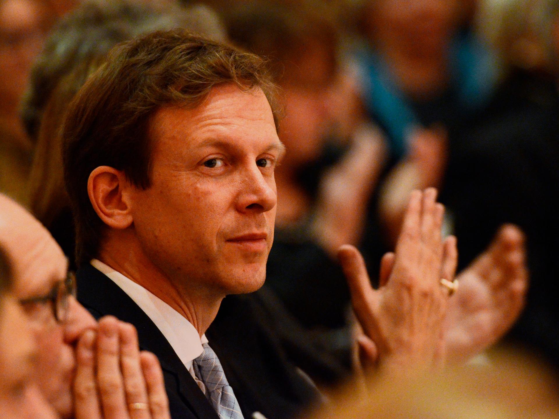 Porträt von Ronald Reng, der Anzug trägt und zwischen einer Reihe von anderen Menschen sitzt.