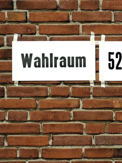 Zettel mit dem Hinweis auf einen Wahlraum kleben auf einer Backsteinwand.