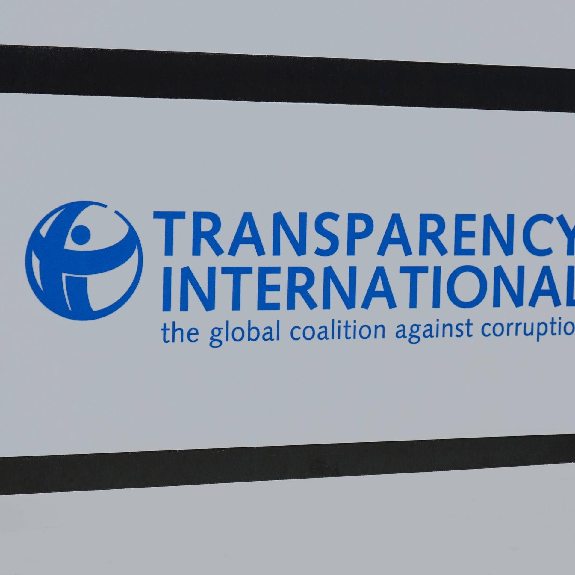 Auf einem Schild befindet sich das Logo und der Schriftzug von Transparency International.