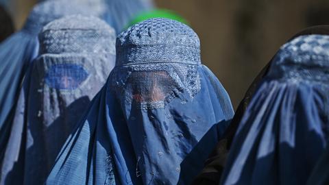 Eine Gruppe von vollverschleierten Frauen stehen hintereinander in einer Schlange.