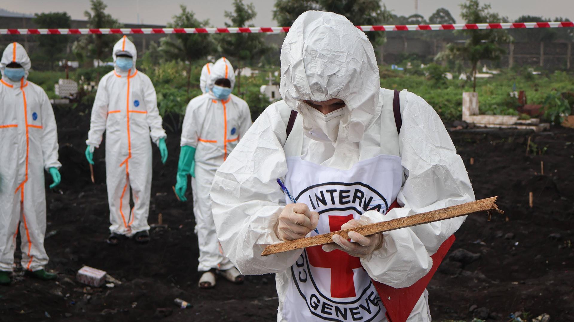 In Schutzanzüge verhüllte Helfer des Internationalen Roten Kreuzes (IRK) bergen die Toten nach Häuserkämpfen in der kongolesischen Millionenstadt Goma. Eine Person steht im Vordergrund, andere arbeiten weiter hinten. 